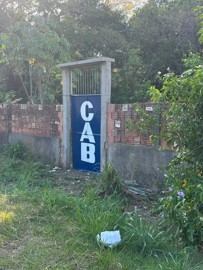 Portão de pedestres azul com as letras CAB, encaixado no muro de tijolos do terreno