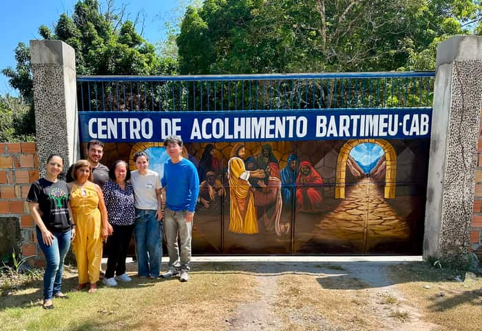Grupo de seis voluntários posando lado a lado diante do portão principal do CAB